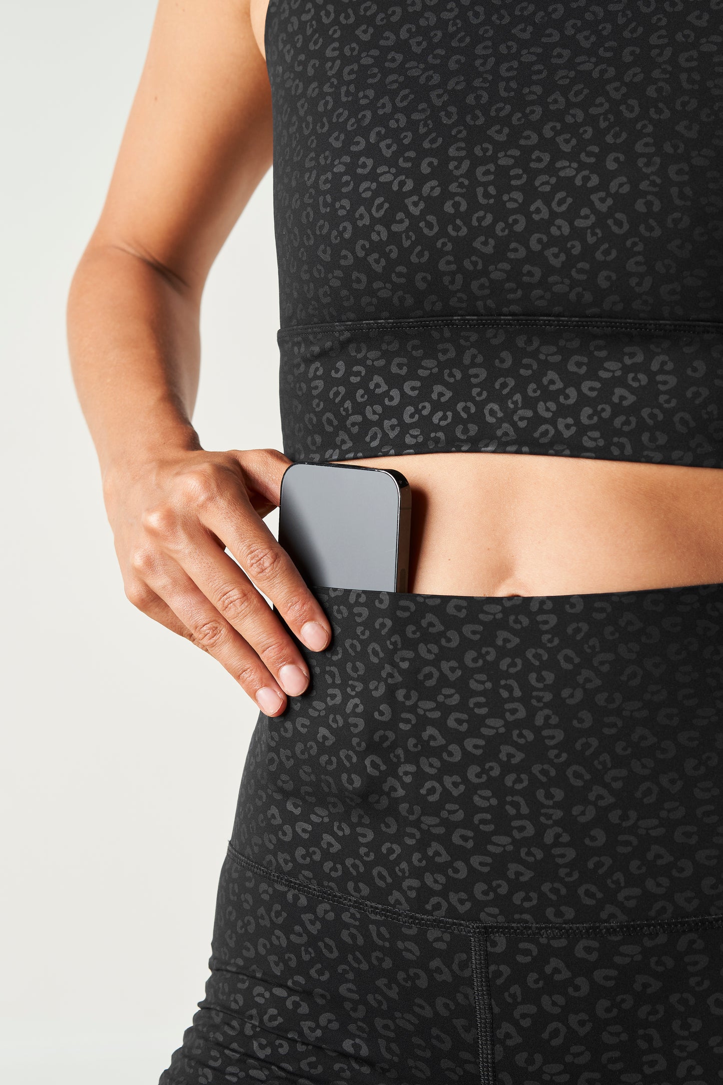 Modèle portant le legging et la brassière The Fierce en noir avec imprimé léopard, conçu avec un tissu compressif certifié OEKO-TEX et notre technologie MicroPerle® pour stimuler le drainage lymphatique, améliorer la circulation, réduire la fatigue et lisser la peau. Legging de compression