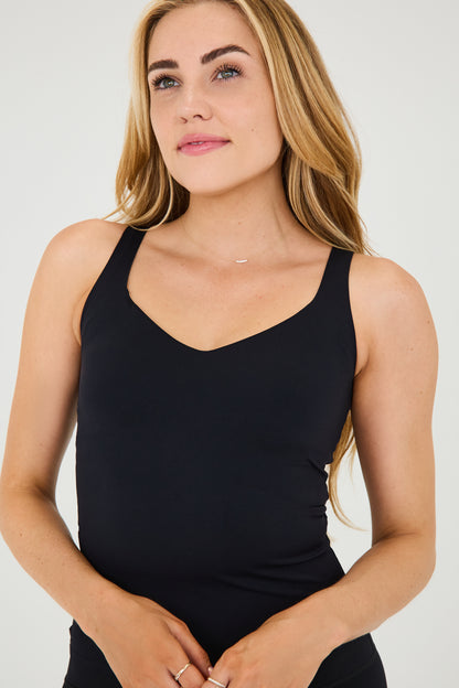 Modèle portant le débardeur Iconic noir, à la coupe sculptante et compressive, avec une encolure élégante et une brassière intégrée. Conçu avec des MicroPerle® le long du dos pour stimuler la circulation lymphatique et favoriser une bonne posture, ce débardeur au design épuré passe facilement du sport à une tenue plus habillée.