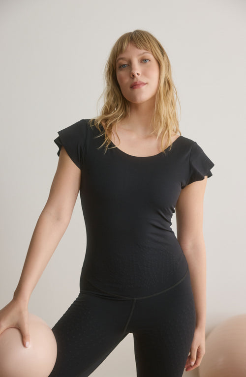 Charger l&#39;image 1 dans la galerie. La combinaison Le Cha-Cha, de couleur noire, présente un dos échancré sophistiqué, des manches délicates et une silhouette épurée. Fabriquée avec un tissu de compression certifié OEKO-tex, notre technologie MicroPerle® favorise le drainage lymphatique, améliore la circulation, réduit la fatigue et booste la vitalité.