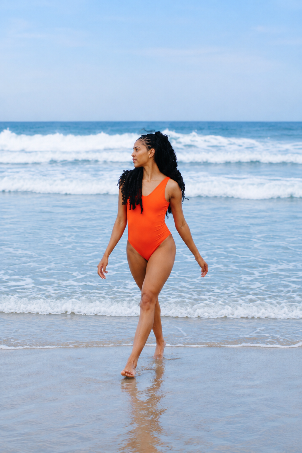 Modèle portant le body Adorn coloris coquelicot, issu de la collection sculpturale Adorn d’Elastique. Il présente un décolleté flatteur bordé de festons, un dos nu et une silhouette lisse et ajustée, conçue pour être portée en maillot ou au quotidien. Confectionné dans un tissu UPF 50 et infusé de MicroPerle® brevetées pour une stimulation lymphatique douce et un maintien ciblé du centre du corps.