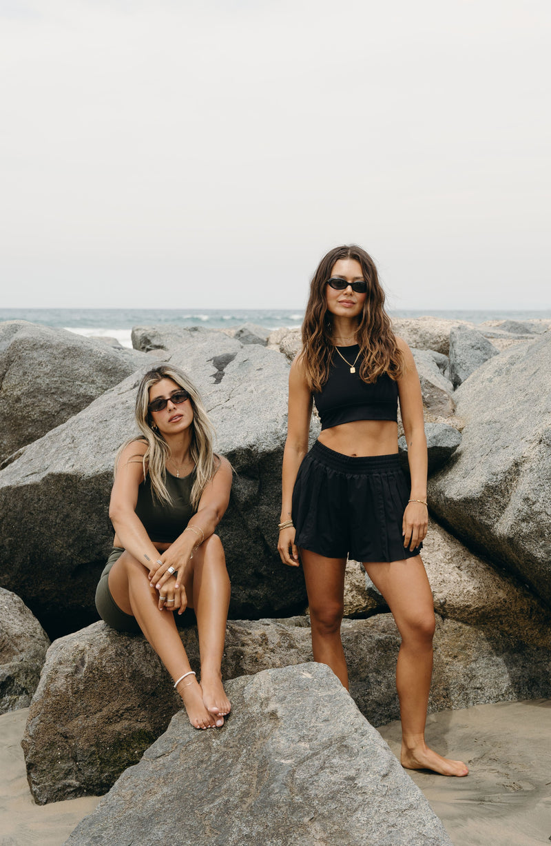 Modèle portant le short L’Original Flowy, composé d’une couche extérieure plissée ultra-légère et d’un short intérieur gainant à effet sculptant. Ce design 2-en-1 allie élégance féminine et maintien performant, avec l’intégration brevetée de MicroPerle® et une poche intérieure discrète pour y glisser l’essentiel — téléphone ou balle de tennis.