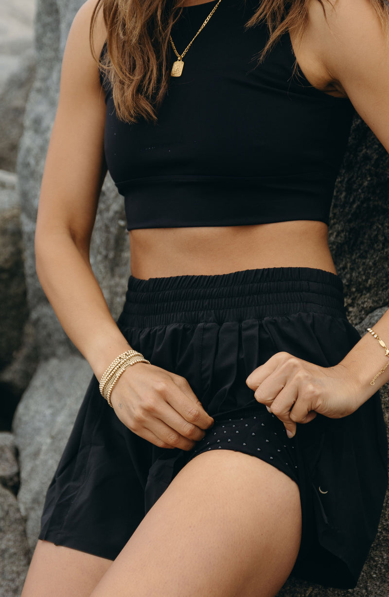 Modèle portant le short L’Original Flowy, composé d’une couche extérieure plissée ultra-légère et d’un short intérieur gainant à effet sculptant. Ce design 2-en-1 allie élégance féminine et maintien performant, avec l’intégration brevetée de MicroPerle® et une poche intérieure discrète pour y glisser l’essentiel — téléphone ou balle de tennis.