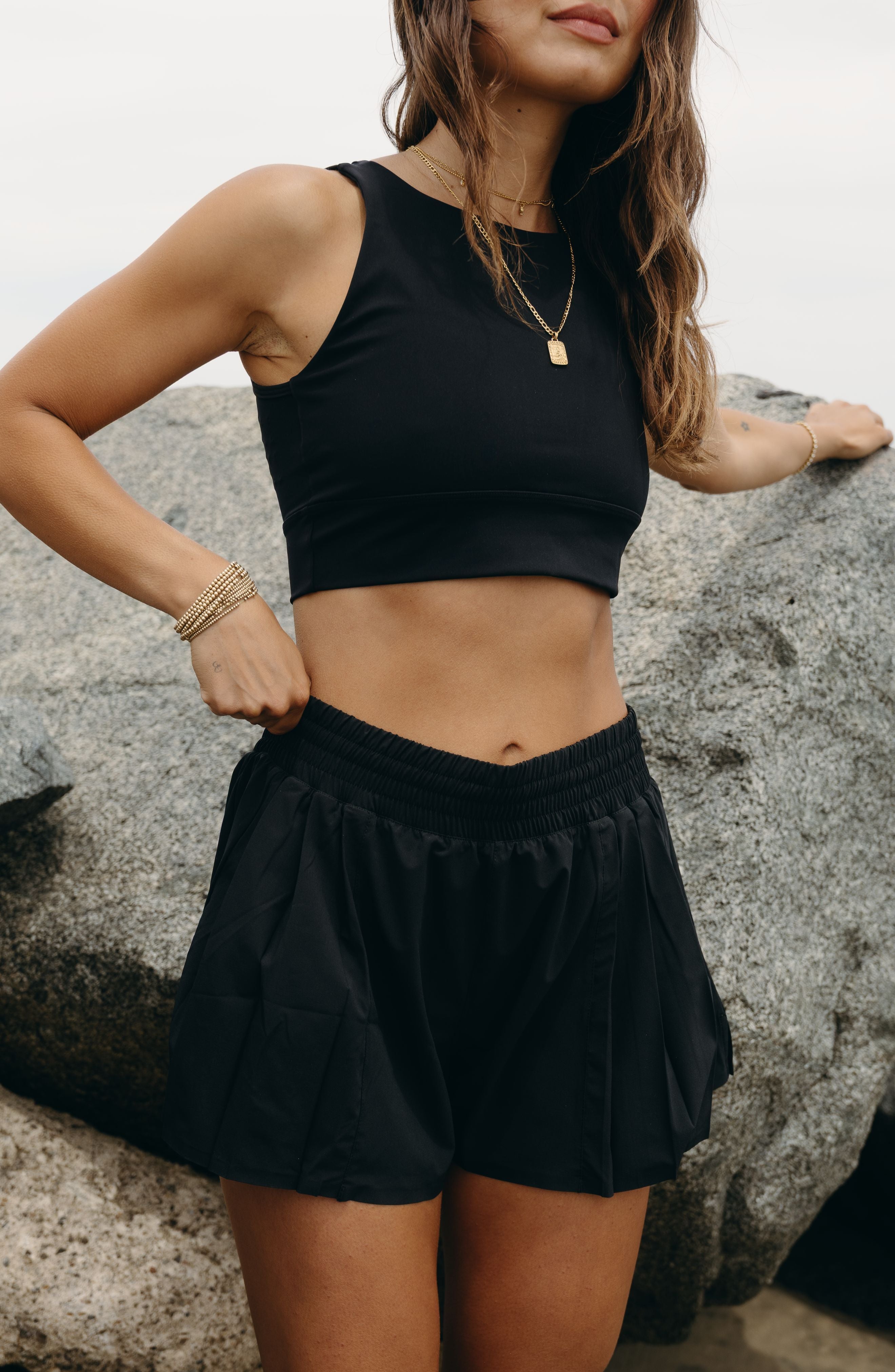 Modèle portant le short L’Original Flowy, composé d’une couche extérieure plissée ultra-légère et d’un short intérieur gainant à effet sculptant. Ce design 2-en-1 allie élégance féminine et maintien performant, avec l’intégration brevetée de MicroPerle® et une poche intérieure discrète pour y glisser l’essentiel — téléphone ou balle de tennis.