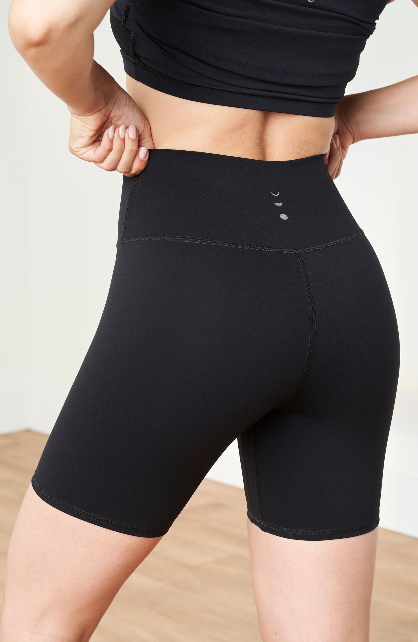 Mannequin portant le short de cyclisme Lisse assorti à son soutien-gorge noir, confectionné dans un tissu de compression certifié OEKO-TEX®, conçu pour lisser, sculpter et soutenir le corps afin d’offrir un confort et une circulation optimaux.