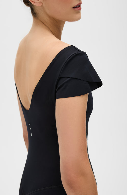 Charger l&#39;image 1 dans la galerie. La combinaison Le Cha-Cha, de couleur noire, présente un dos échancré sophistiqué, des manches délicates et une silhouette épurée. Fabriquée avec un tissu de compression certifié OEKO-tex, notre technologie MicroPerle® favorise le drainage lymphatique, améliore la circulation, réduit la fatigue et booste la vitalité.