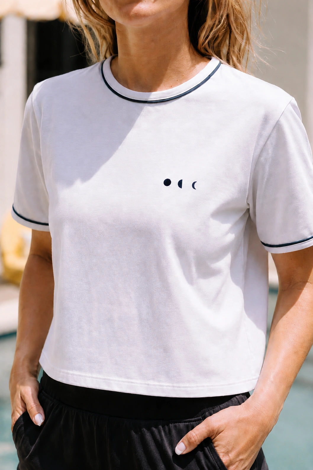 Gros plan du crop tee blanc de la collection Monte Carlo, rehaussé de finitions bleu marine contrastées. Inspiré de l’univers balnéaire haut de gamme, ce modèle allie confort au quotidien, allure sportive élégante et style raffiné au bord de la piscine.