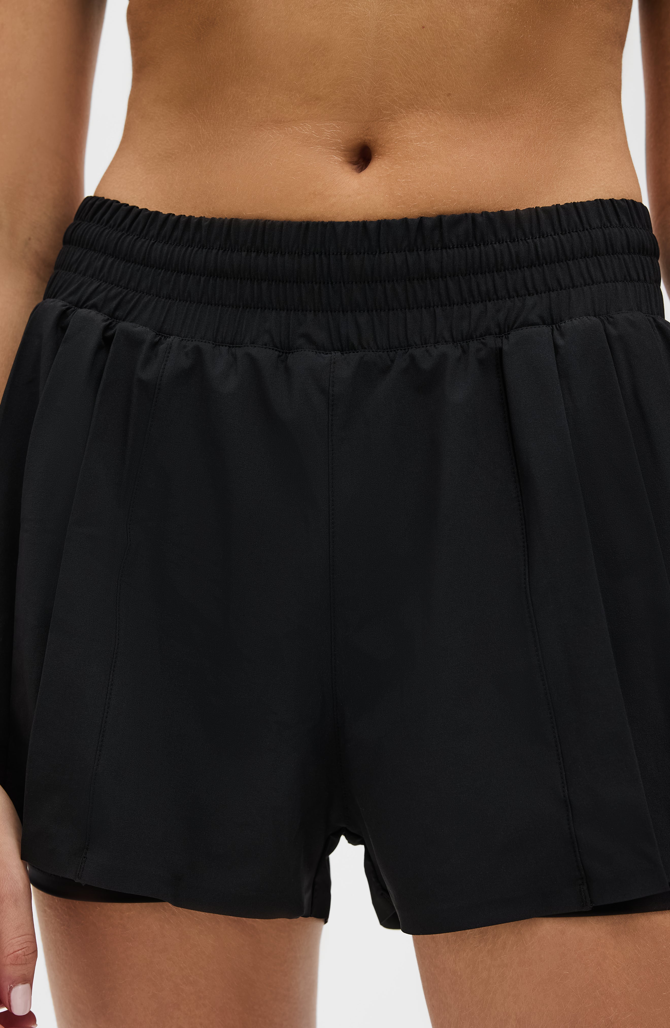 Modèle portant le short L’Original Flowy, composé d’une couche extérieure plissée ultra-légère et d’un short intérieur gainant à effet sculptant. Ce design 2-en-1 allie élégance féminine et maintien performant, avec l’intégration brevetée de MicroPerle® et une poche intérieure discrète pour y glisser l’essentiel — téléphone ou balle de tennis.